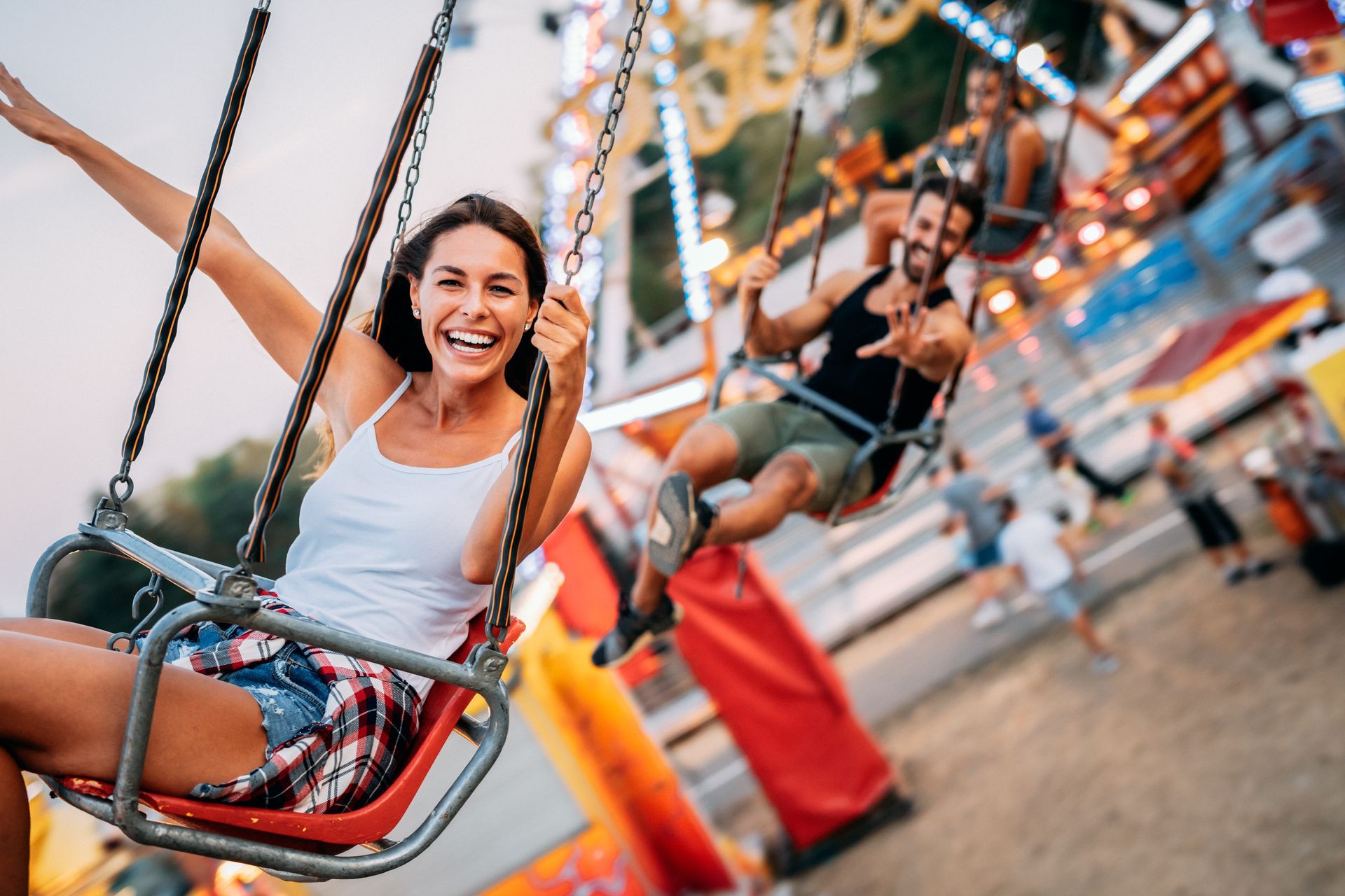 A woman and a man are riding swings at a carnival.