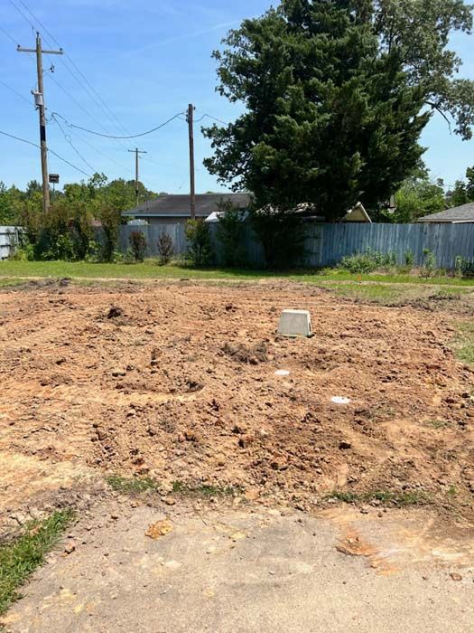 Brown dirt lot with utility box, power lines, and fence in the background under a blue sky.