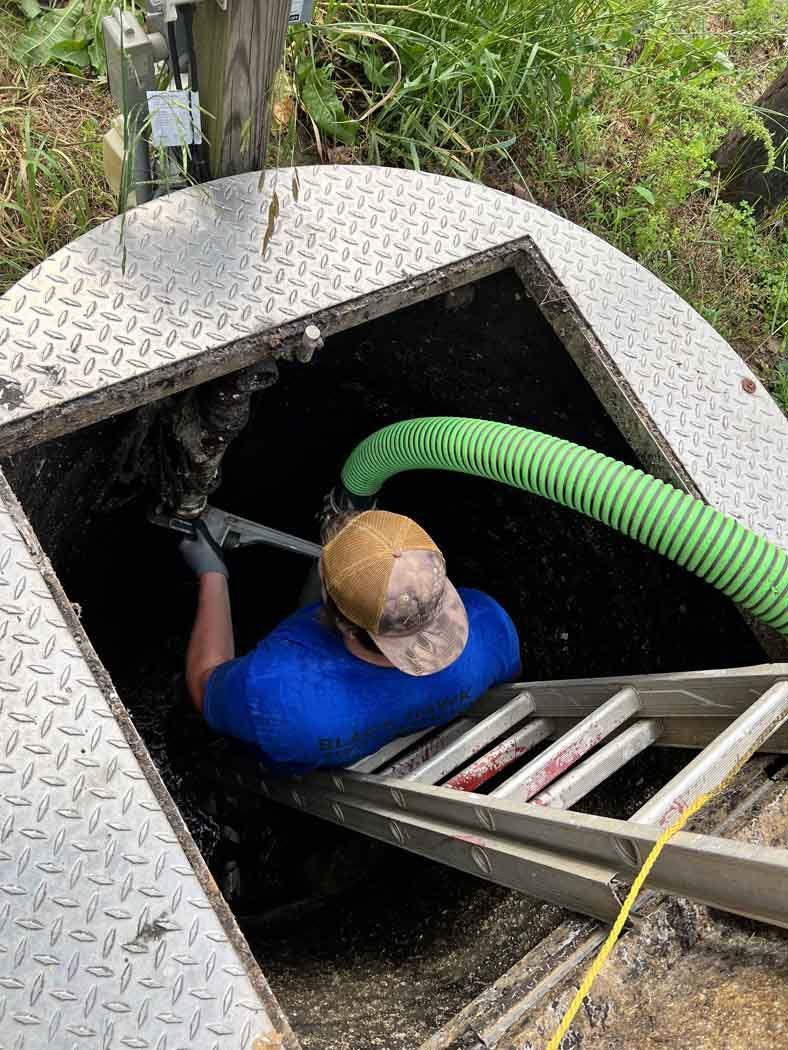 Man inside a septic tank, holding a tool with a green hose nearby.