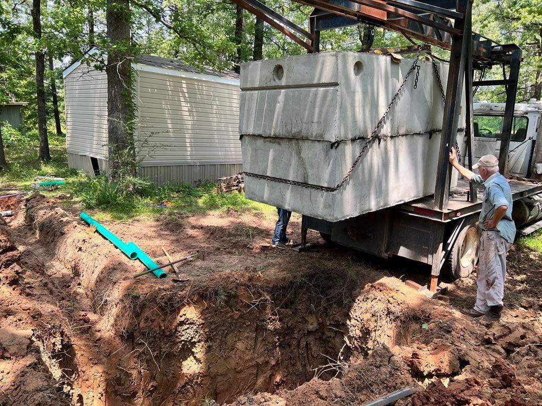 Septic tank being lowered into a large excavated hole beside a mobile home by a truck-mounted crane.