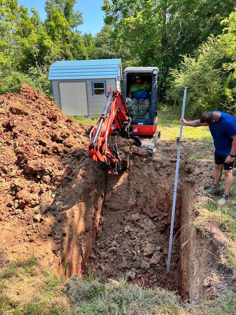 An excavator digs a trench. A man uses a leveler, while another operates the machinery near a small shed.