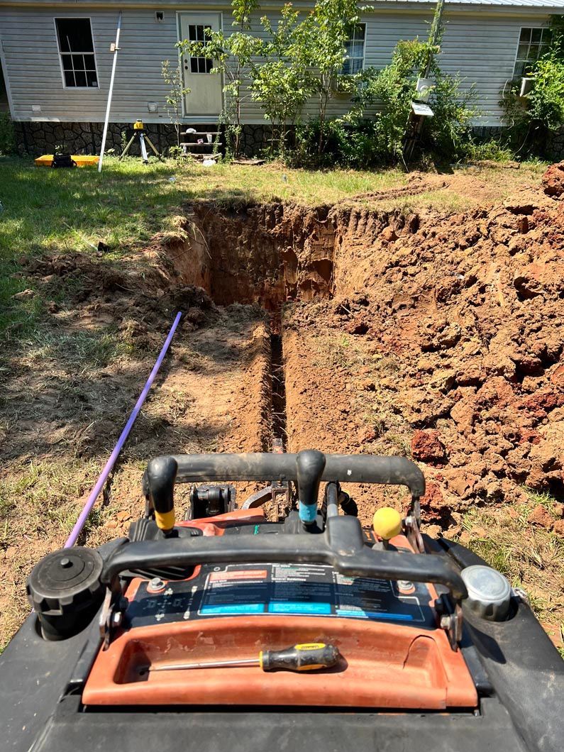 Trench dug near a house with a tool cart in the foreground and purple pipe visible.