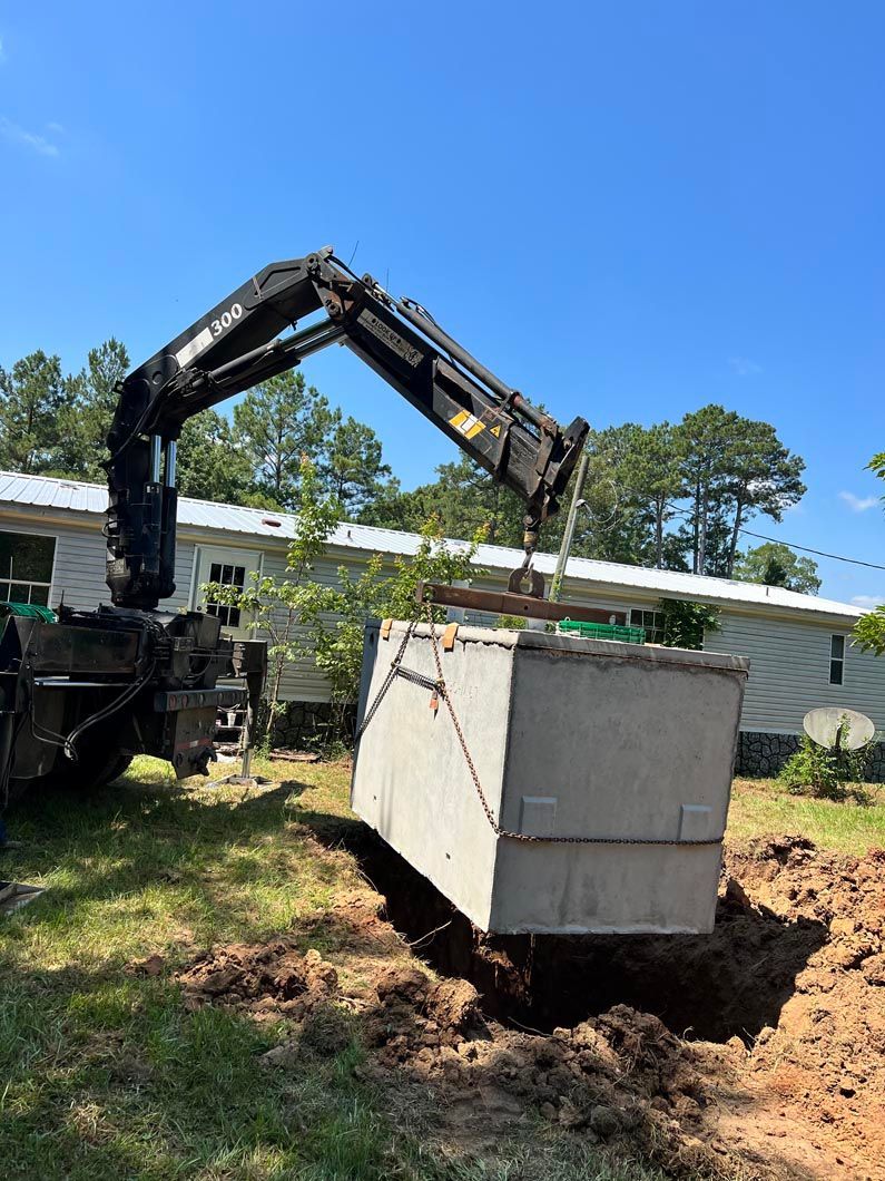 A crane lowers a concrete septic tank into a dug hole in a yard near a house.