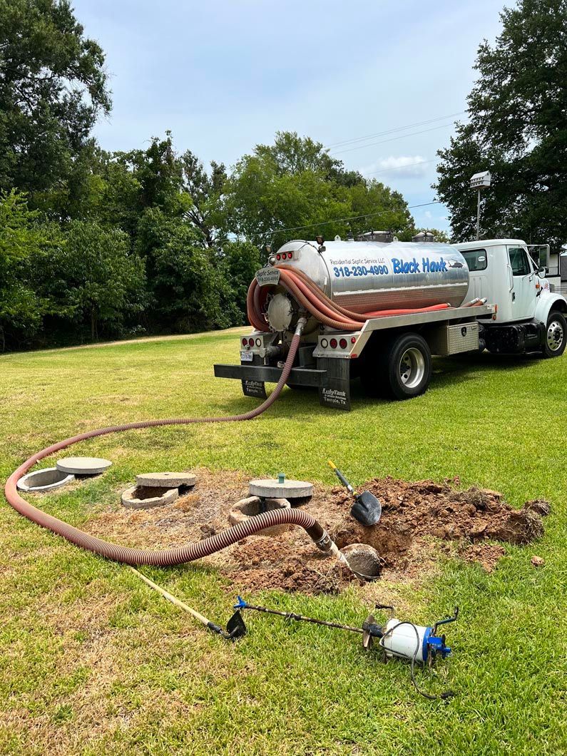 A septic tank pumping truck servicing a septic system in a grassy yard.