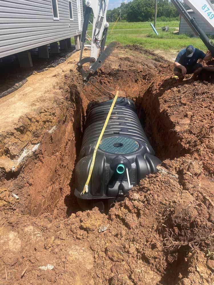 A septic tank installed in a deep trench. A construction worker kneels nearby.