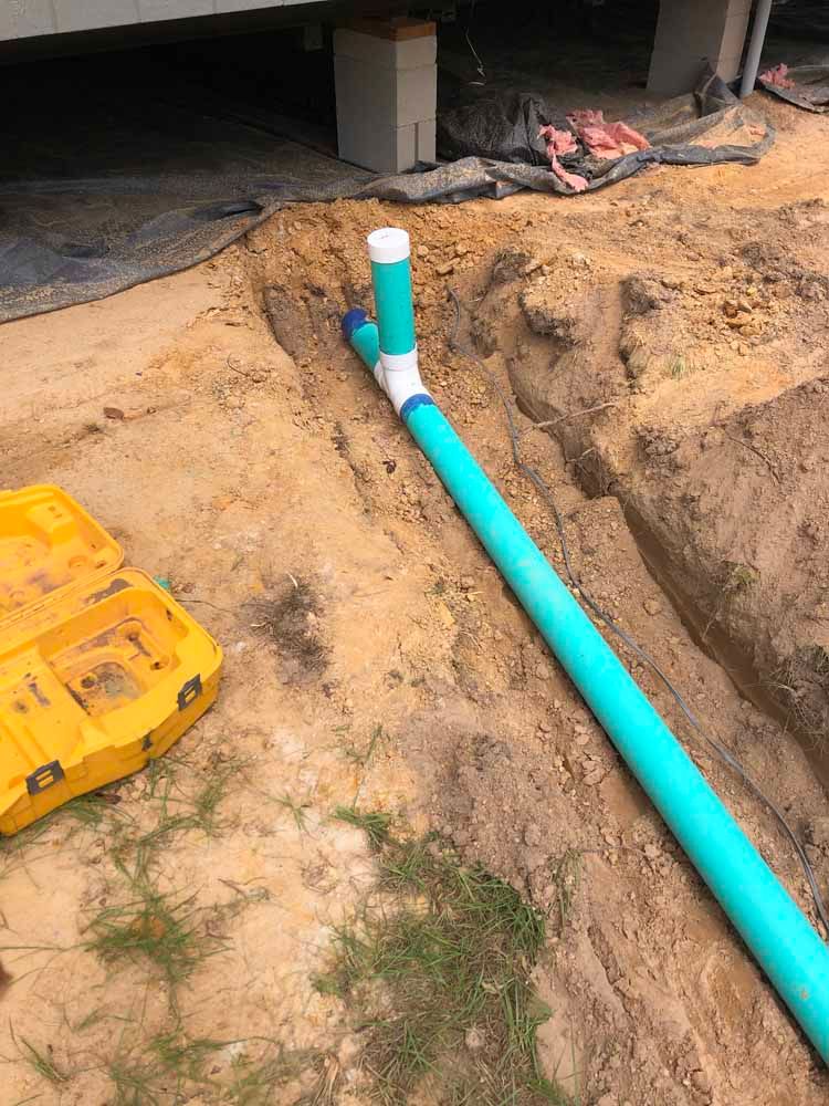 Plumbing pipe installation in sandy soil. Blue and white pipes with a yellow tool box visible.