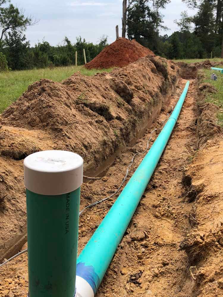 Trench with green pipe, dirt mound, and capped green pipe. Outdoors in a grassy area.