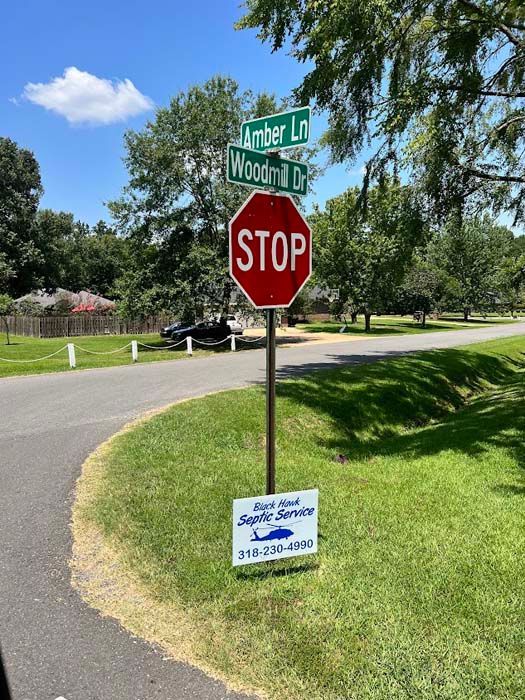 Stop sign at intersection of Amber Ln and Woody Cr, with septic service sign in grassy area.