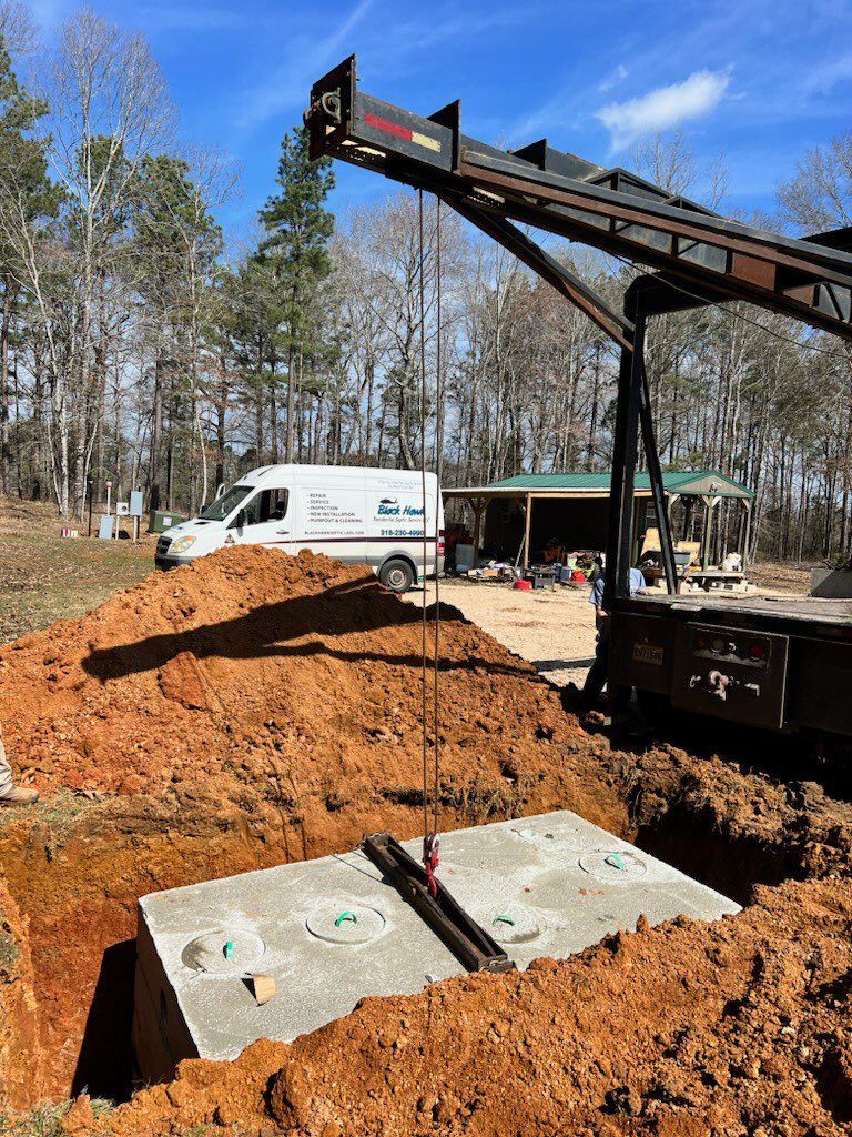 A concrete septic tank being lowered into a trench by a crane on a construction site.