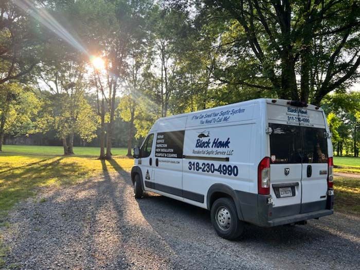 White Black Hawk Mobile Health Service van parked on gravel, trees in background, sunlight.