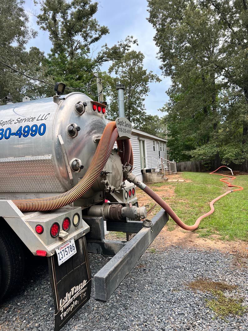 Septic truck pumping a hose onto a lawn; a house and trees are in the background.
