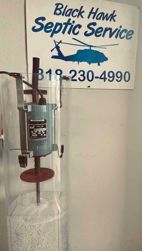 Black Hawk Septic Service sign with a demonstration apparatus inside, showing a component with a rotary component.