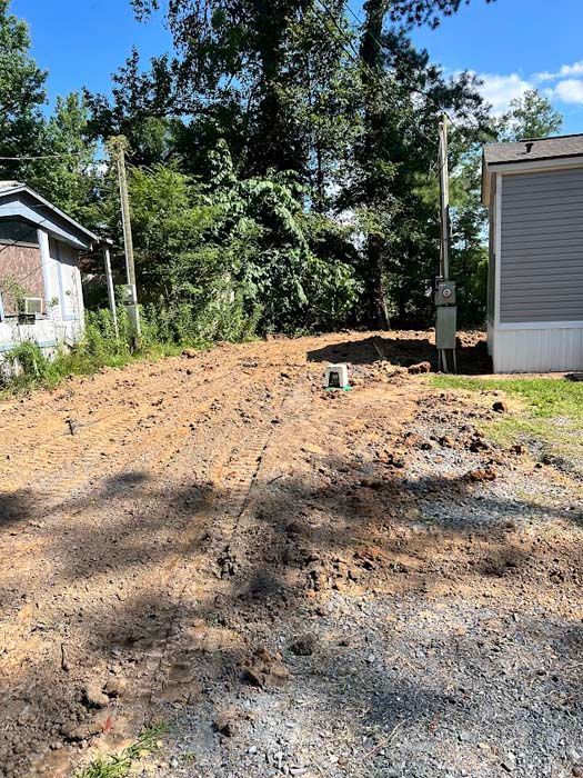 Cleared dirt lot between two buildings, with power pole and trees in the background.