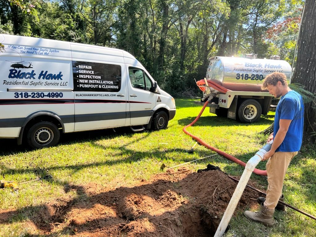 Man pumping septic tank in yard; Black Hawk truck and tanker; green grass and trees.