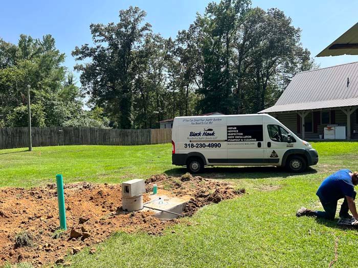 A work van parked in a yard with a man working near a septic system; sunny day.