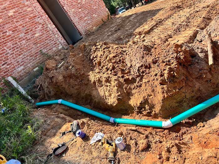 Excavation with turquoise pipes installed near a brick building.