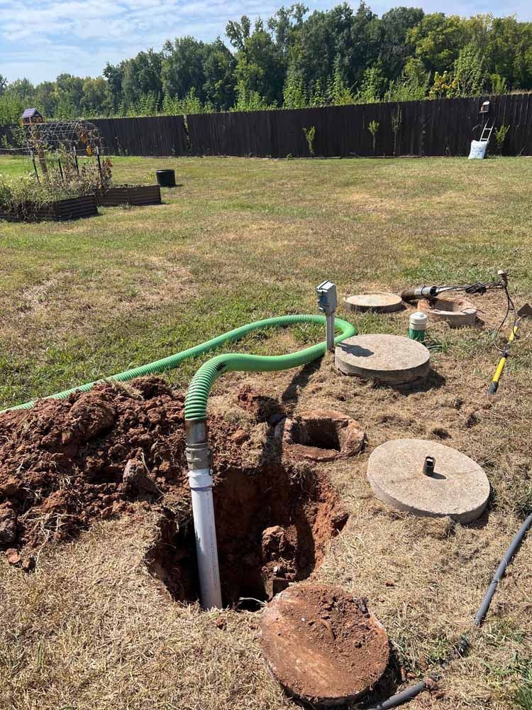 A well-drilling site with a hose, a pipe in the hole, and concrete access covers on grass.