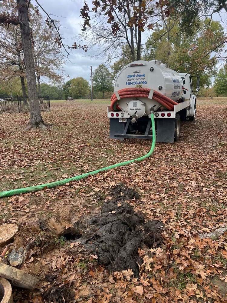 Septic tank truck pumping waste from a hole in a yard with fallen leaves.