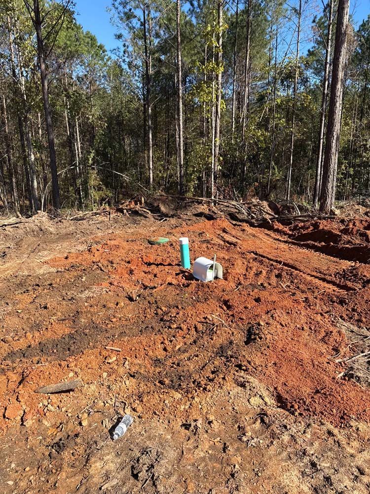 Dirt clearing with a blue pipe and white box, trees in the background.