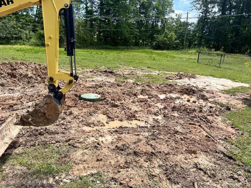 A yellow excavator digs in muddy soil in a grassy field.