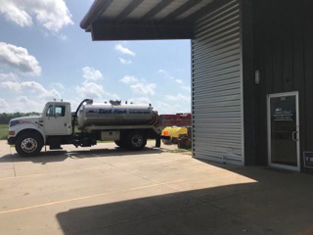 White tanker truck parked outside a building on a sunny day.