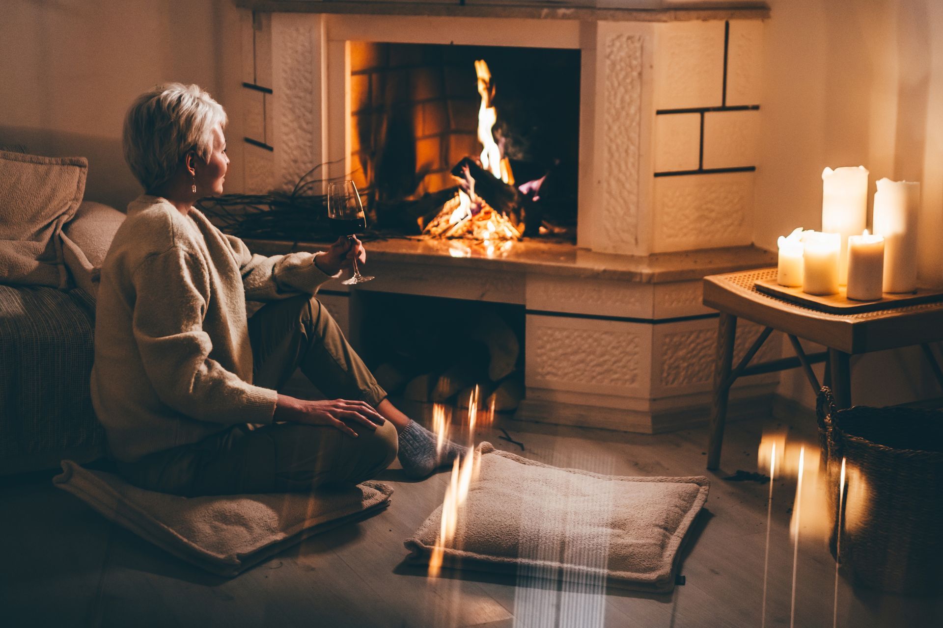 A woman relaxing near a fireplace, drinking red wine.