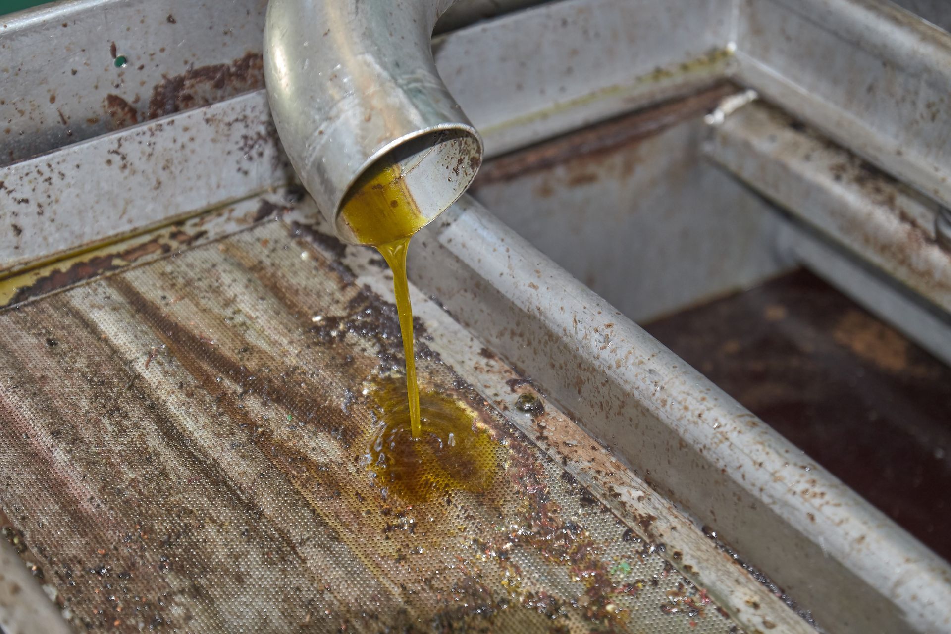 Bright yellow liquid flows from a metal pipe onto a textured, rustic surface in a production setting.