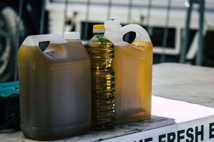 Three containers of cooking oil, including two plastic jugs and one clear bottle, sitting on a surface.