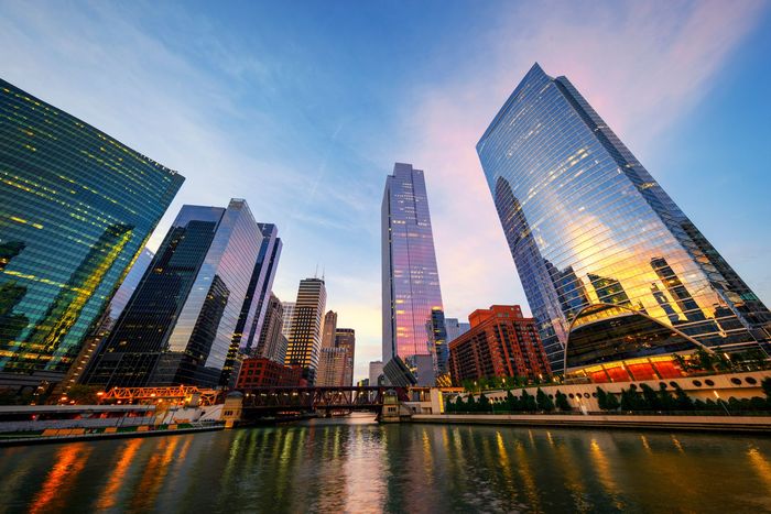 Modern skyscrapers tower over the Chicago River at dusk, their glass facades reflecting the golden sunset.