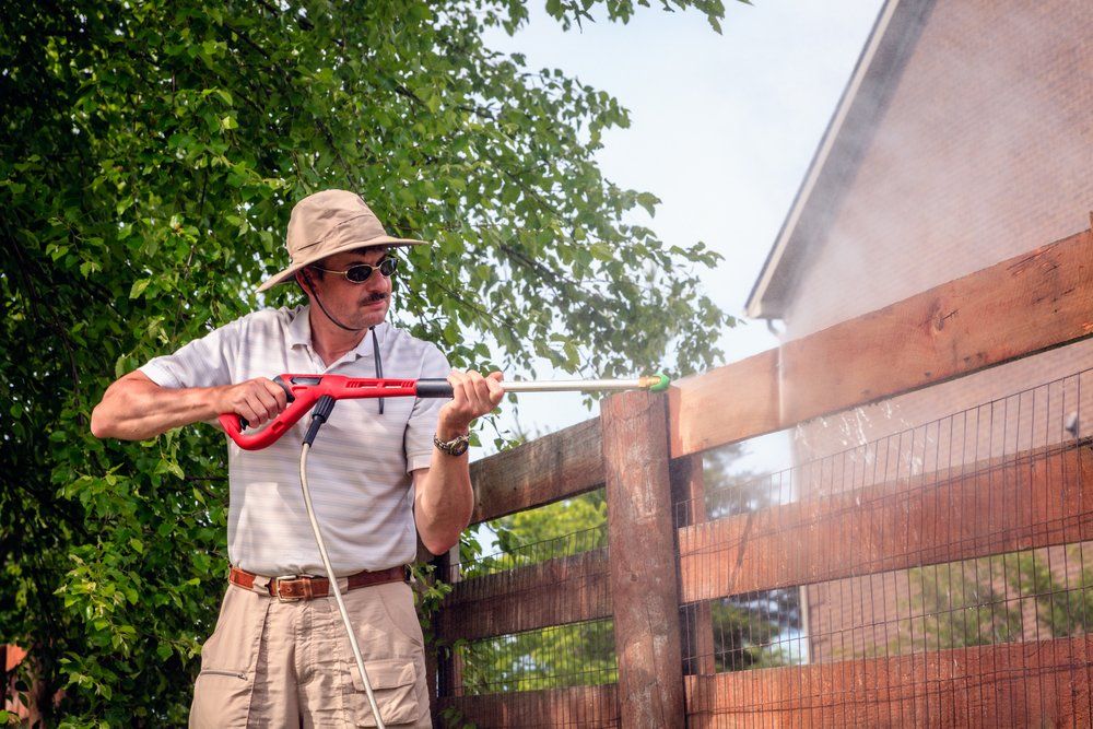 man pressure washing his barn's wooden fence