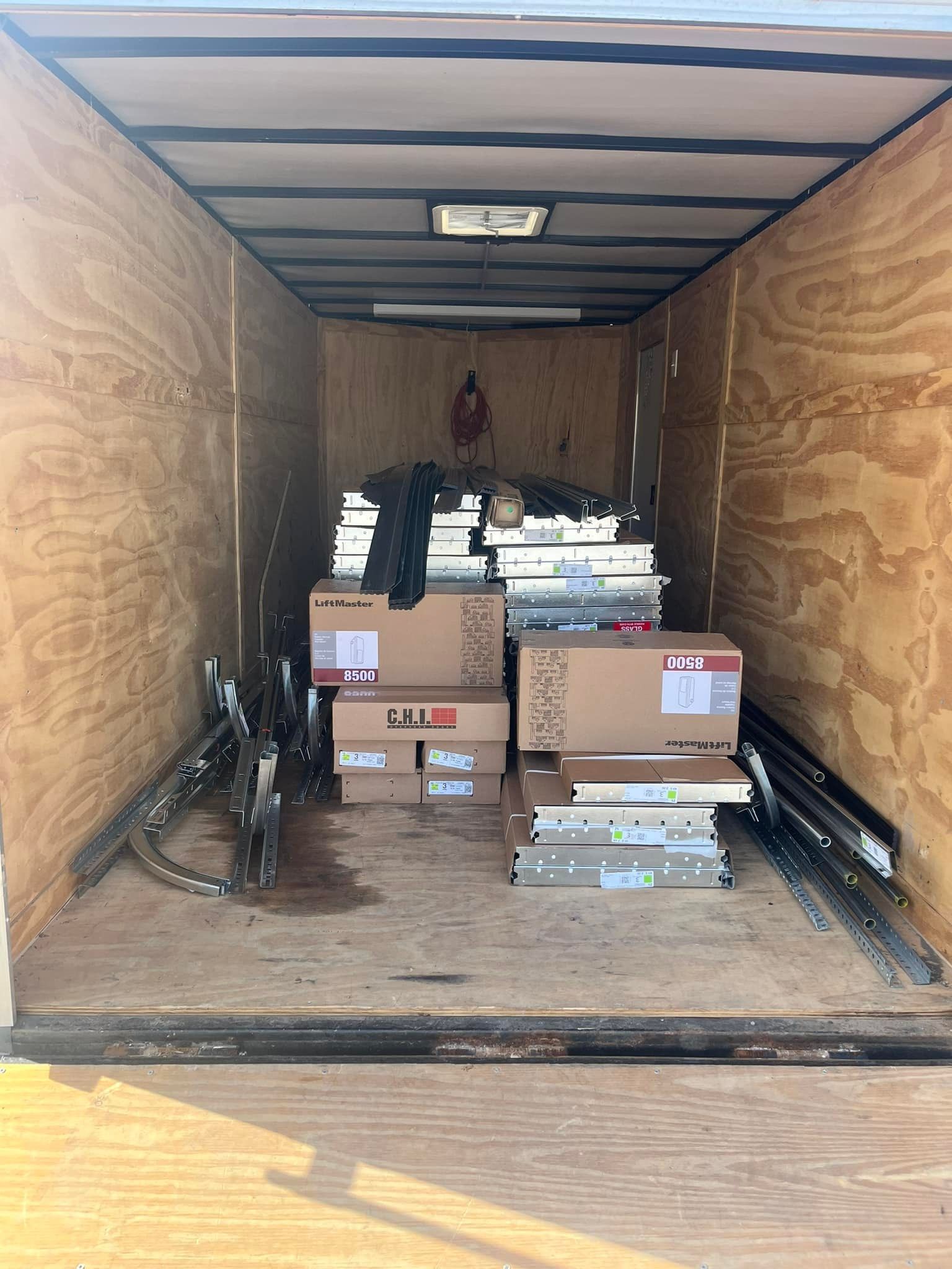 Inside a cargo trailer, boxes and equipment are stored on the wood floor and walls.