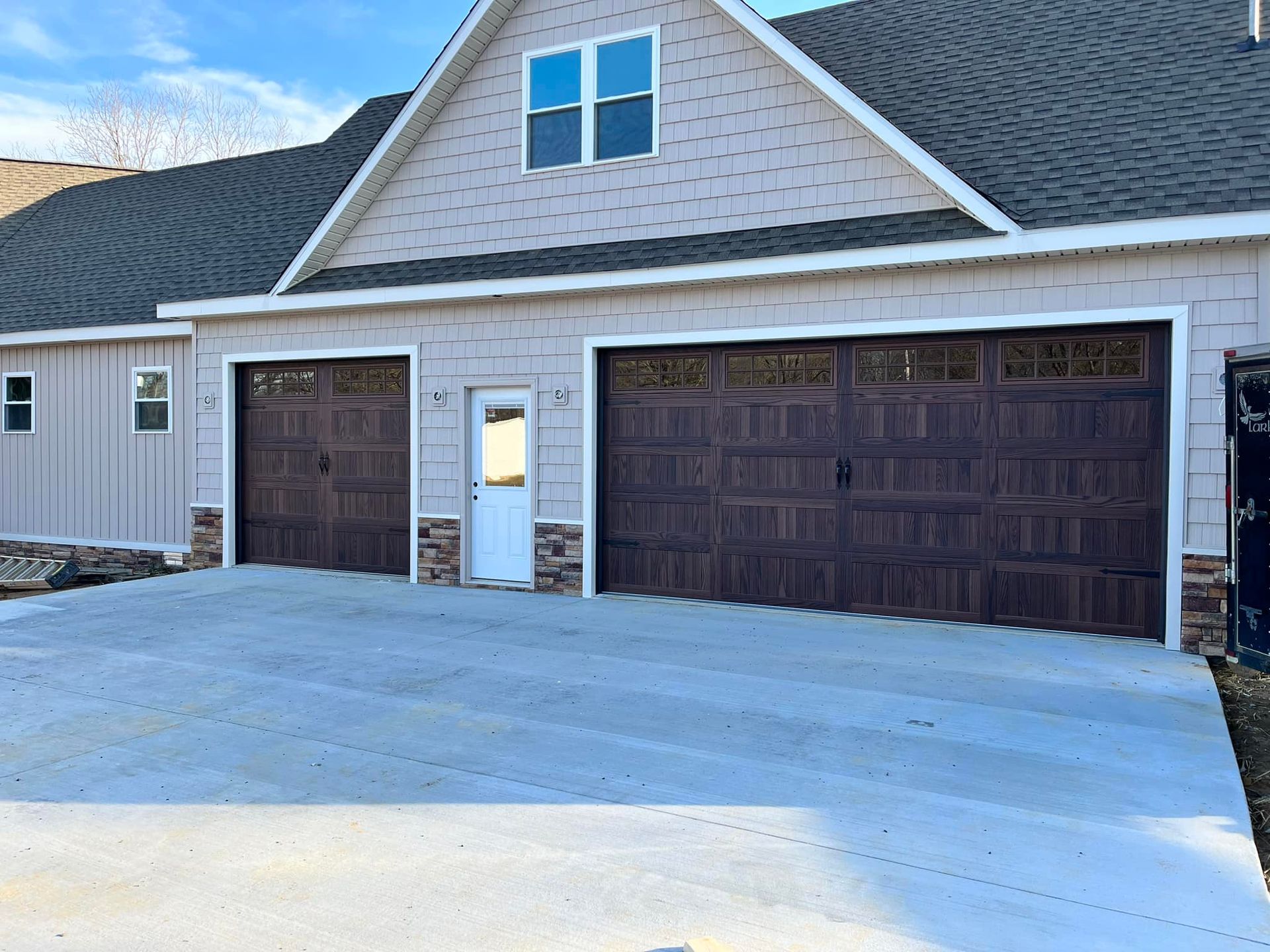 Two-car garage with brown doors, light siding, concrete driveway, and a small white door.