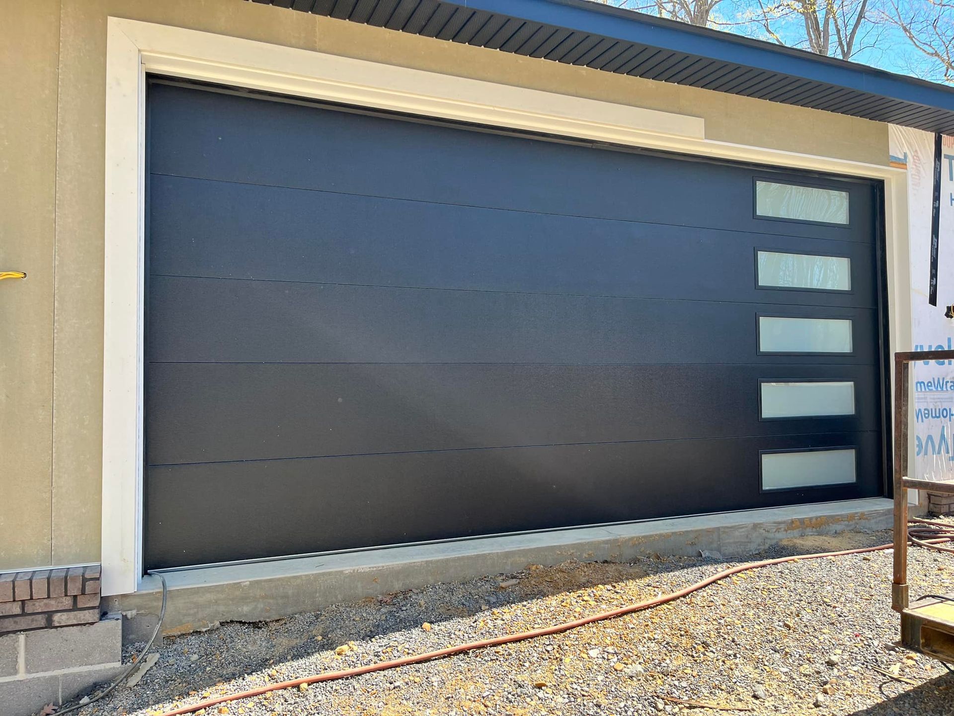 Black garage door with rectangular windows, beige trim, tan exterior.