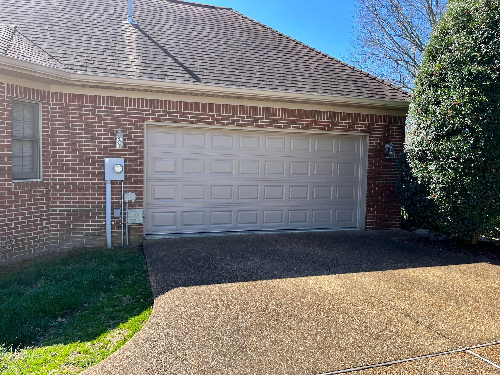 Garage with a beige door, red brick facade, and a concrete driveway.