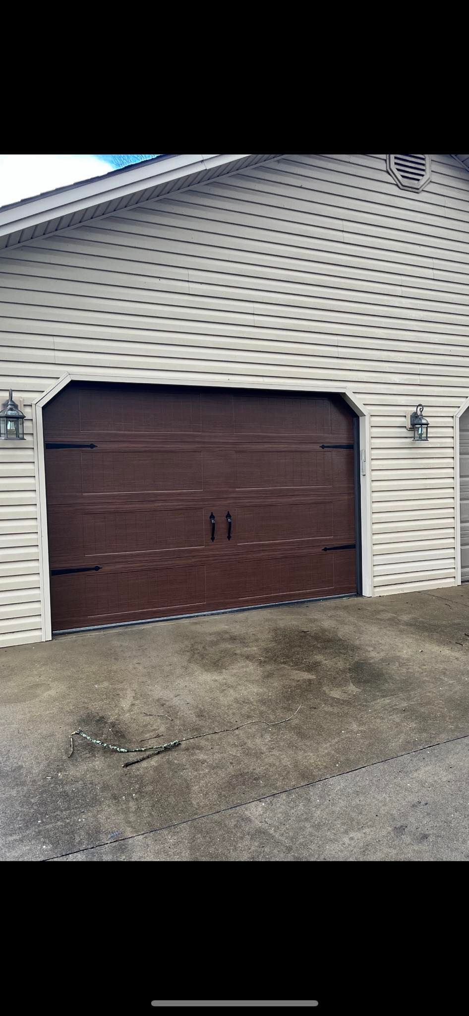 Brown garage door on a house with beige siding; two lights on either side of the door.