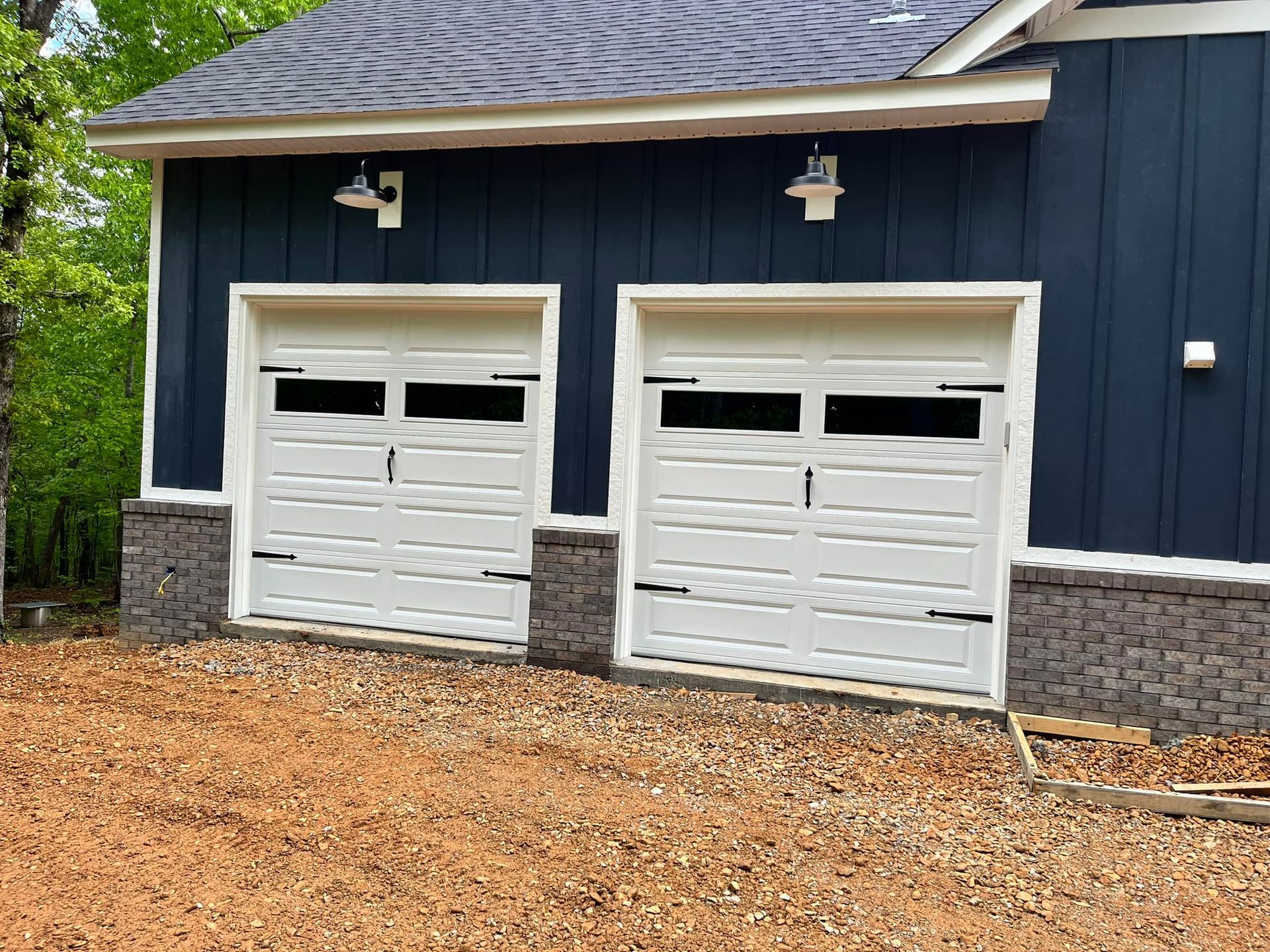 Two white garage doors with black accents on a blue-sided building; mounted lights above.