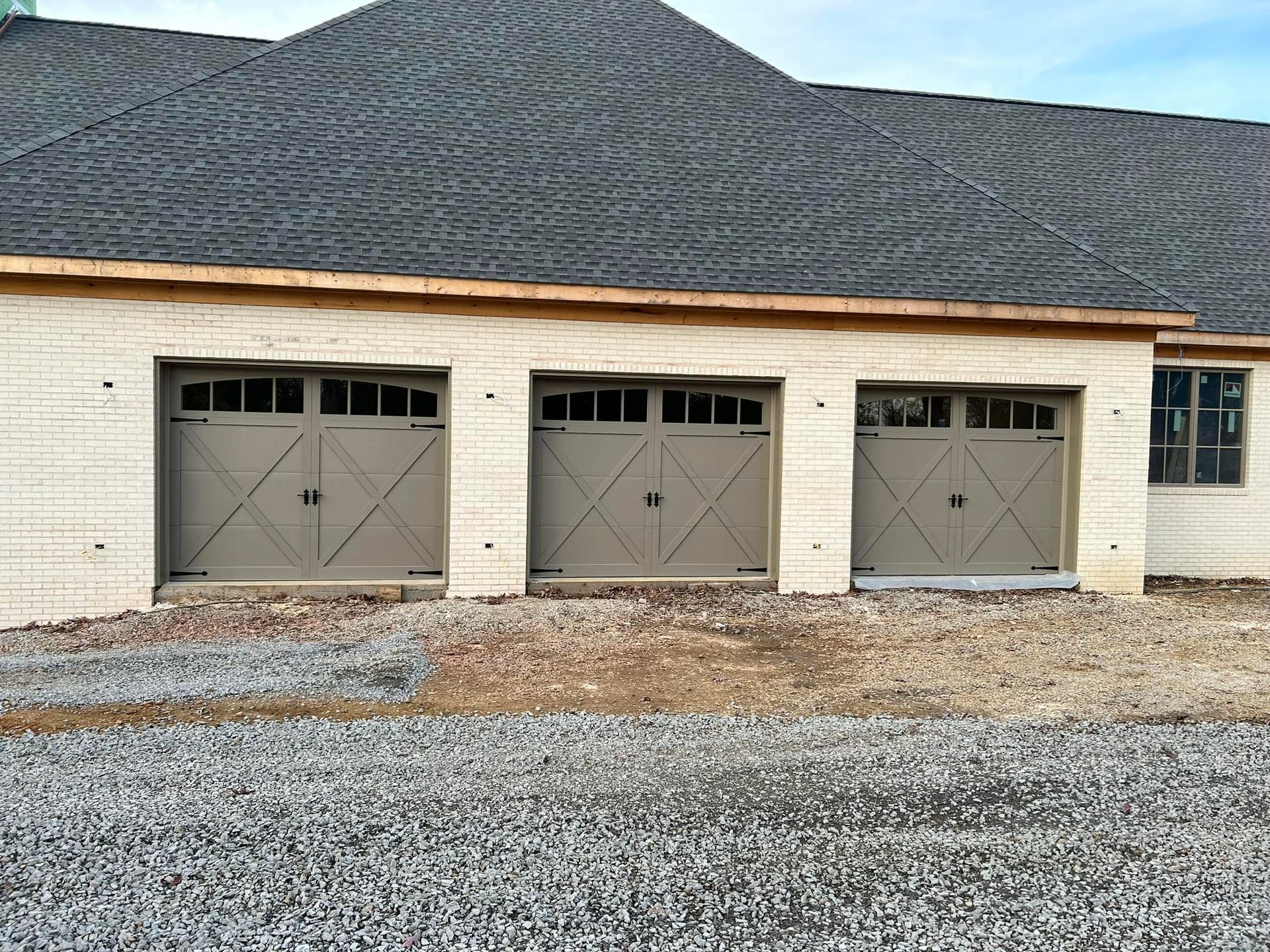 Three-car garage under construction with grey doors, tan facade, and textured dark roof.