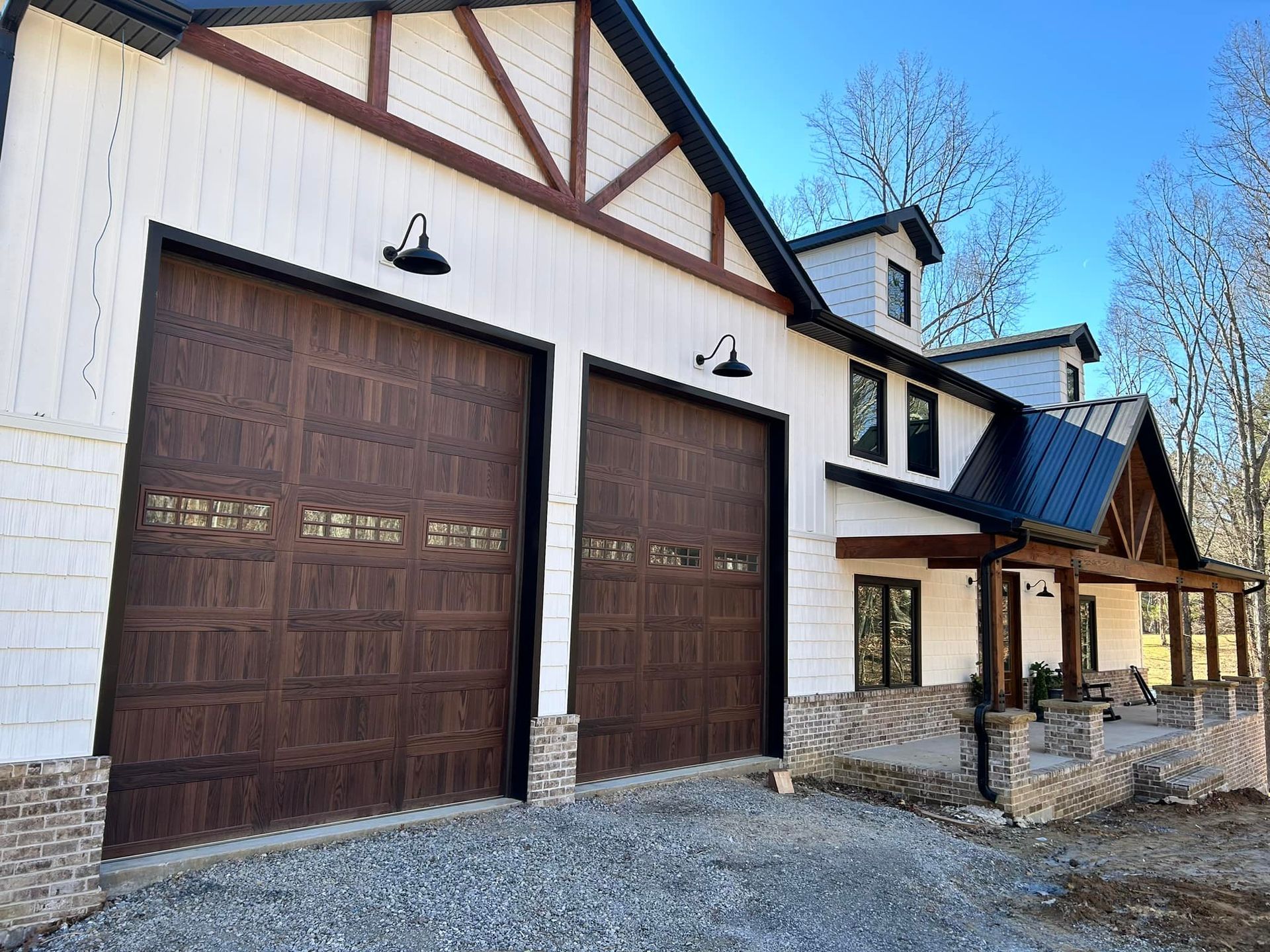 A barn-style house with dark brown garage doors, white siding, and a porch under a blue sky.