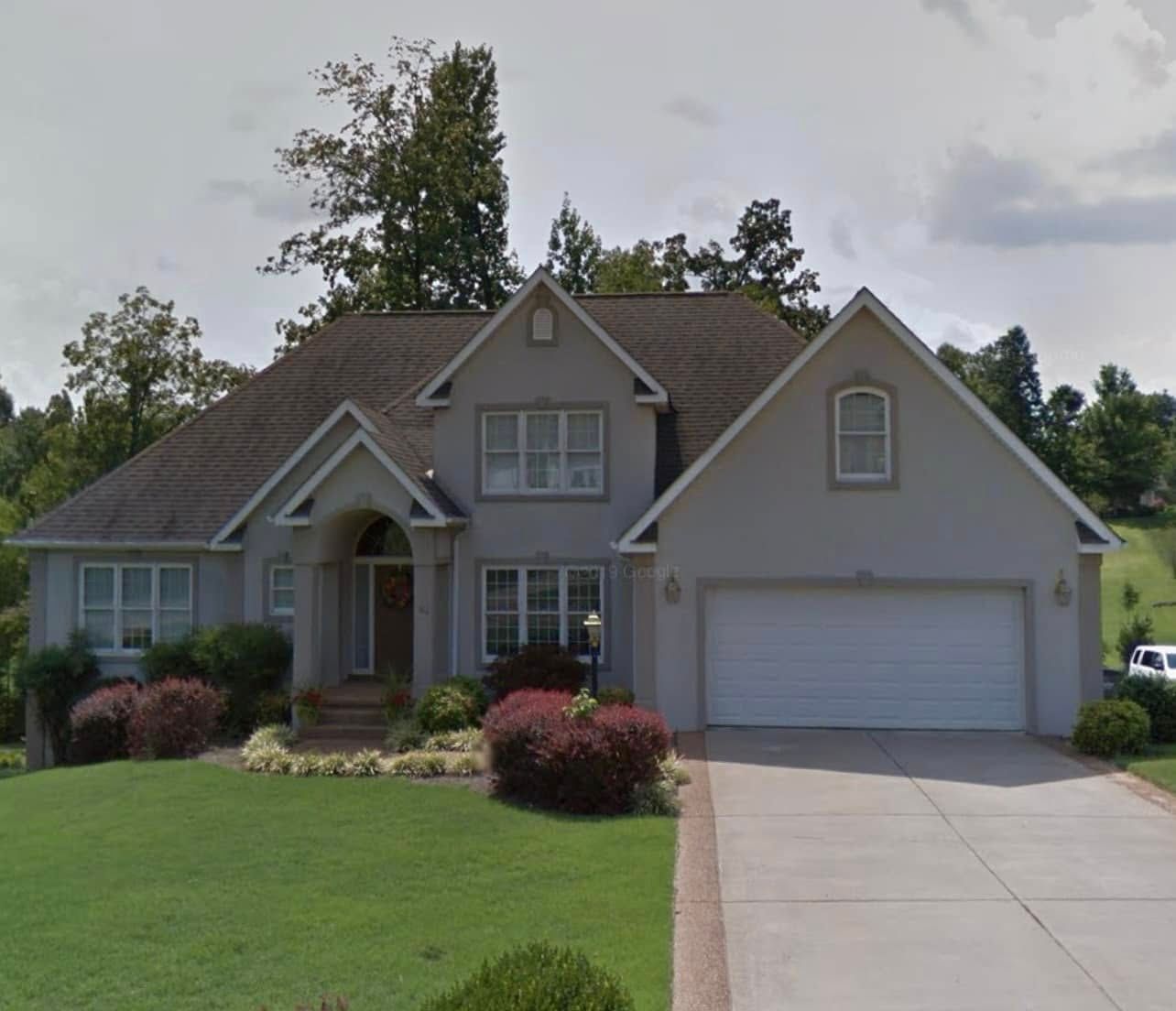 Gray house with a two-car garage, lush lawn, and shrubbery in front.
