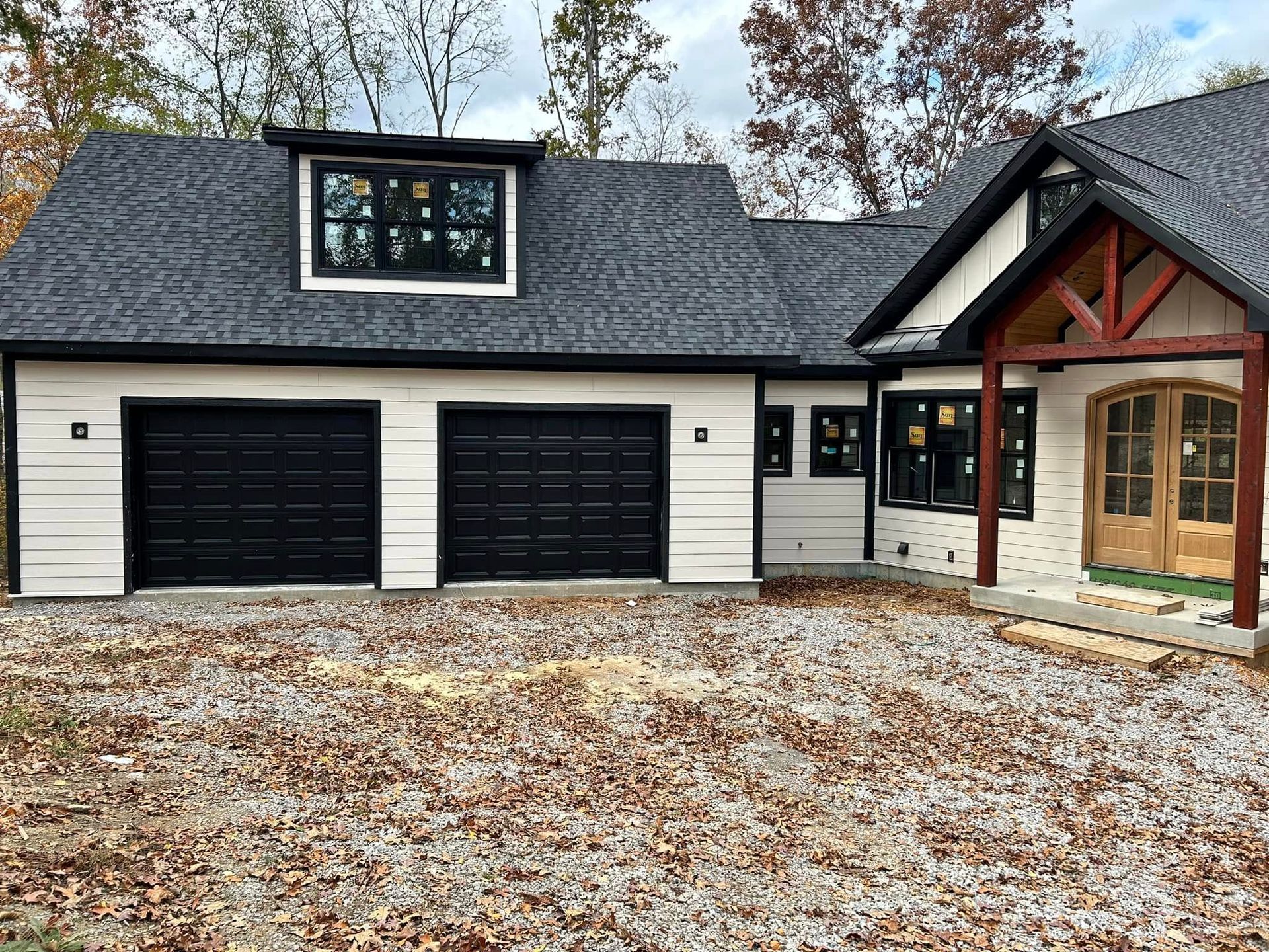 Exterior of a house with black garage doors, white siding, and a brown wood entry.
