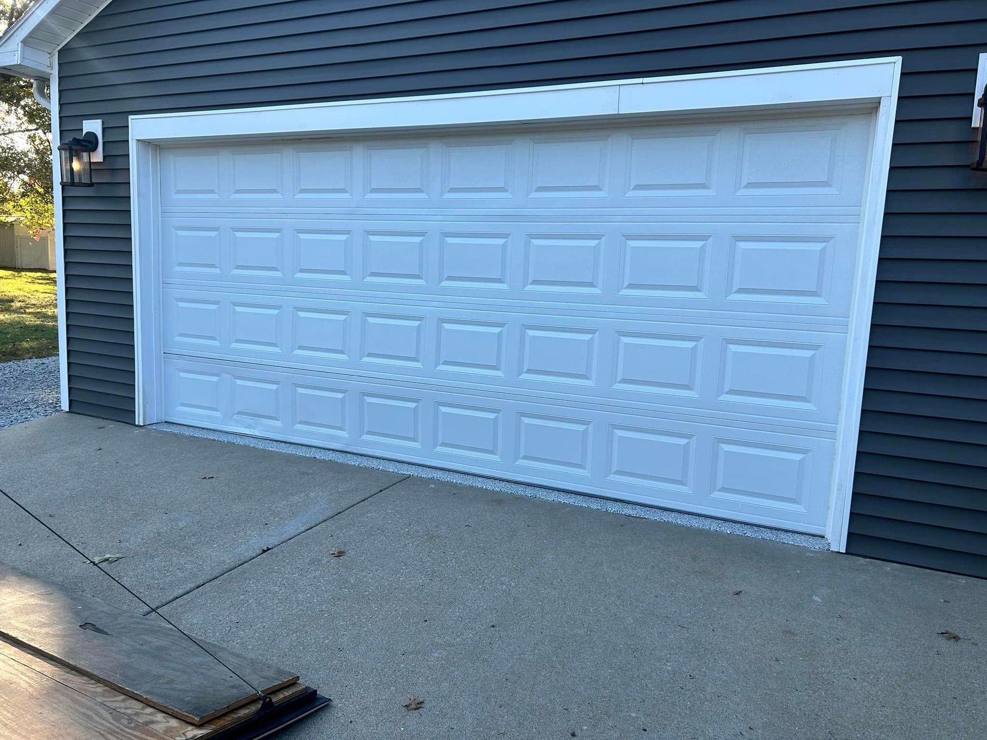 White garage door with square panels, on a gray building with dark siding. Concrete driveway.