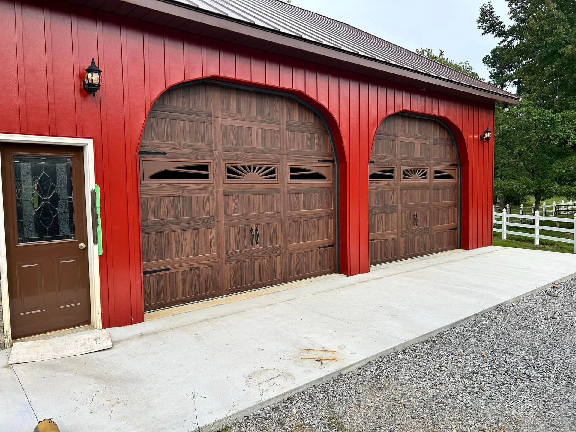 Red barn with brown arched garage doors and a side door.