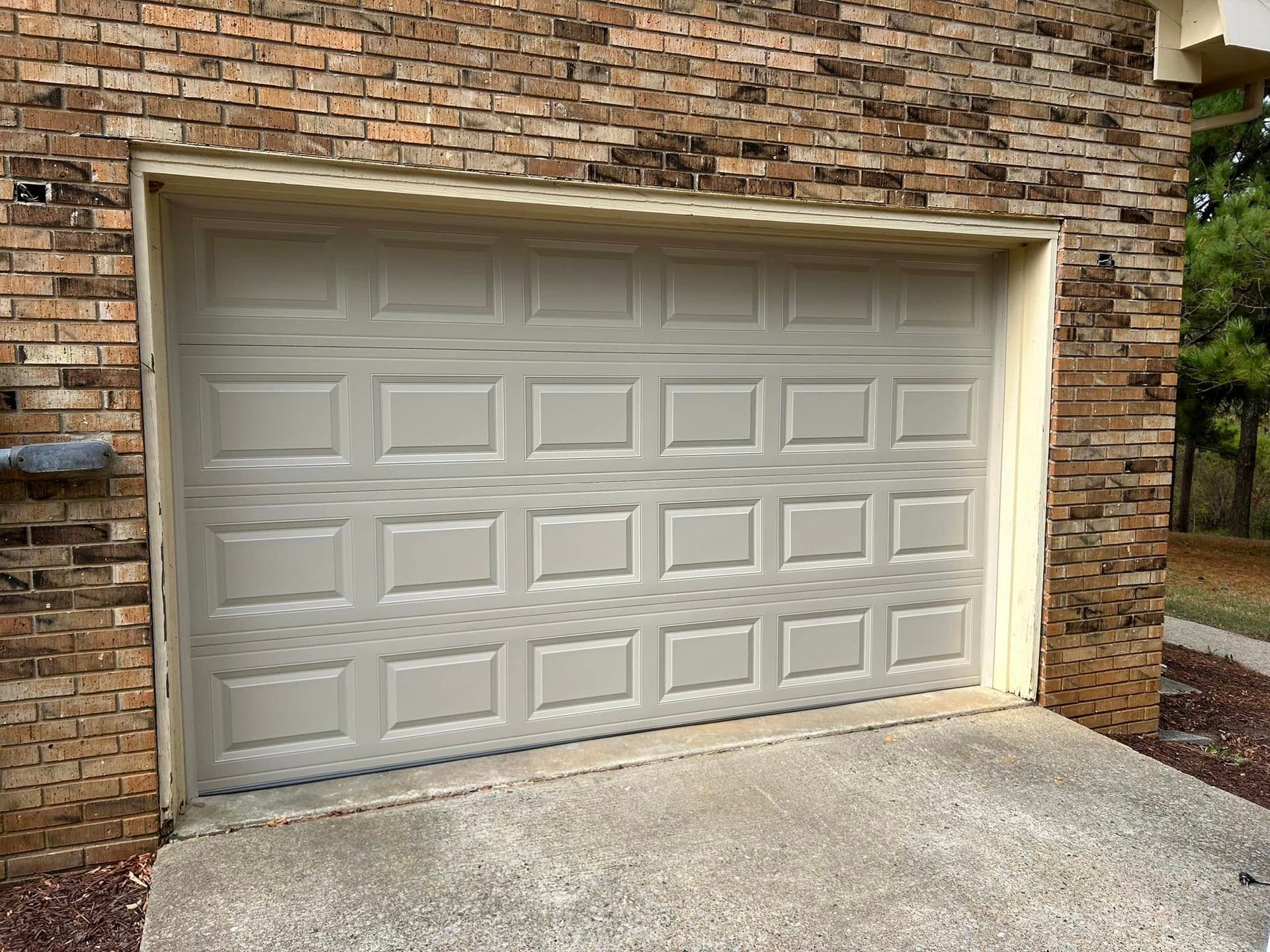 Tan garage door on a brick building with a concrete driveway.