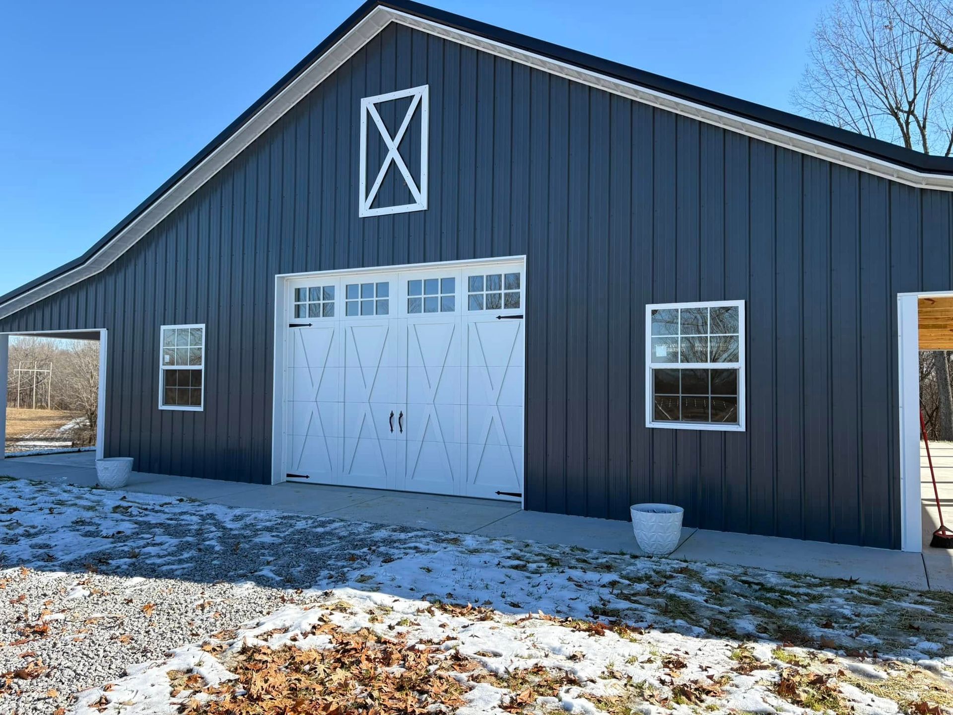 Blue barn with white door and trim, set on a concrete pad on a sunny day.