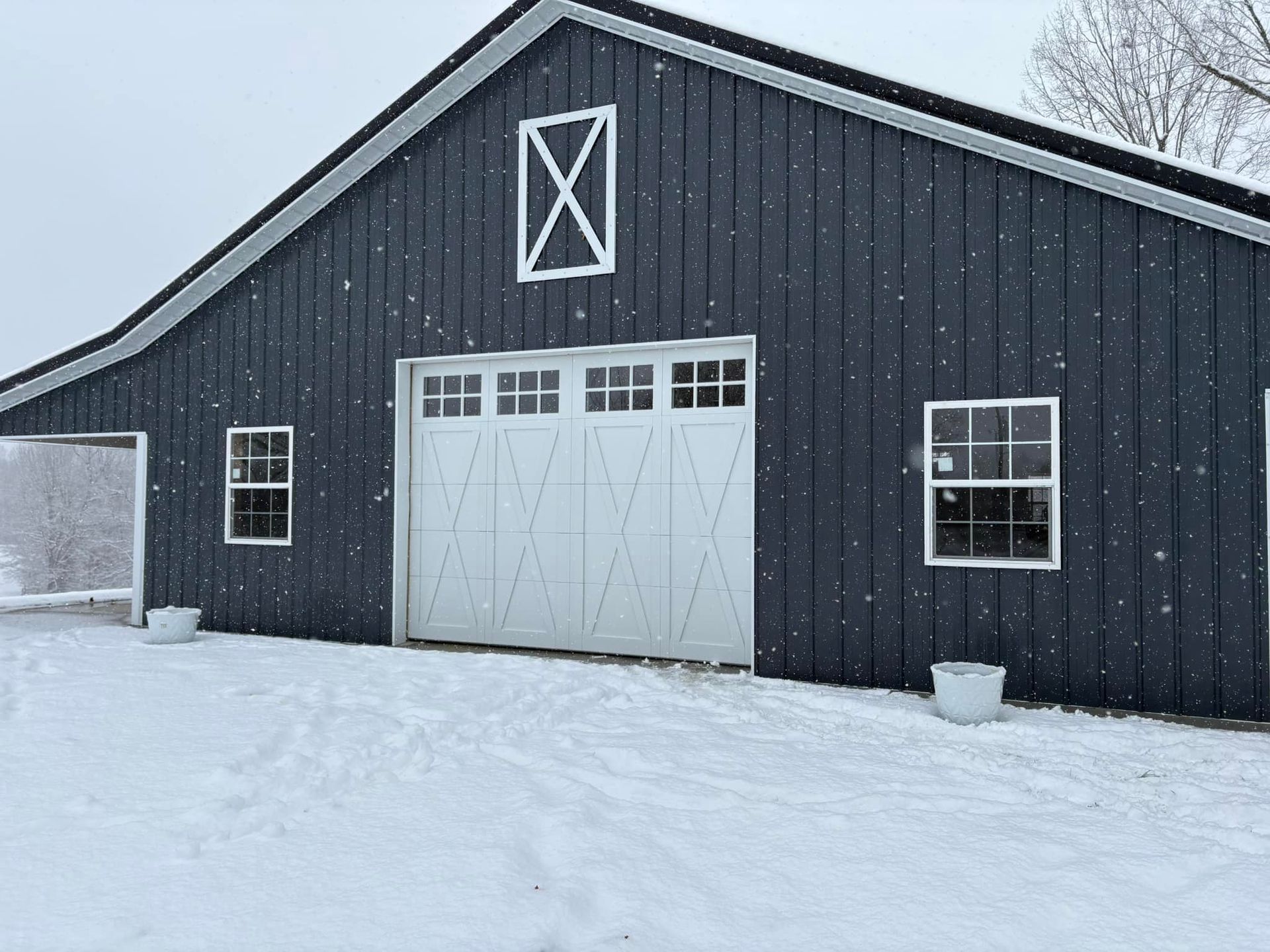 Dark blue barn with white trim, door, and window frames; snow falling in a winter setting.