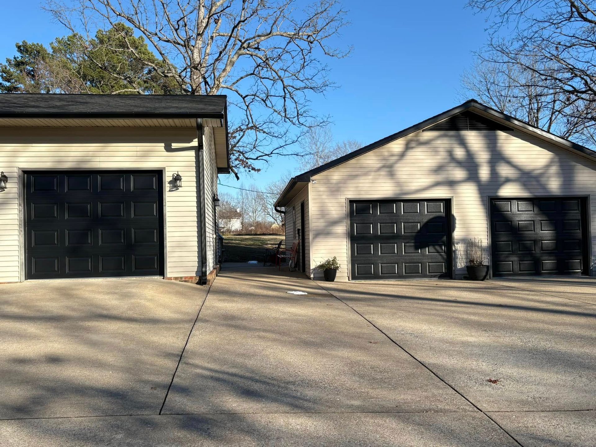 Two beige garages with black doors and a concrete driveway under a blue sky.
