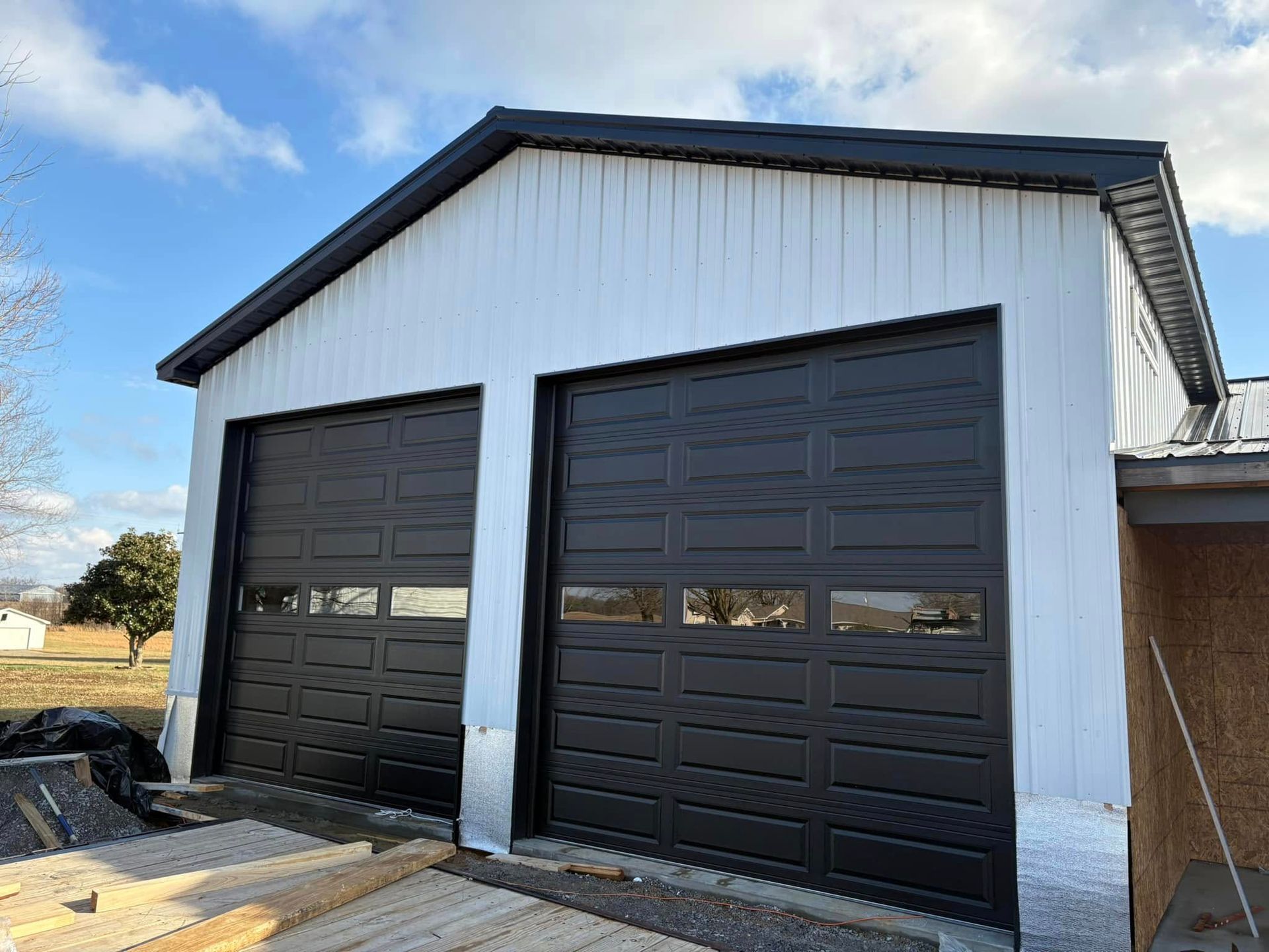 Two-bay garage with black doors, white siding, and a dark roof against a partly cloudy sky.