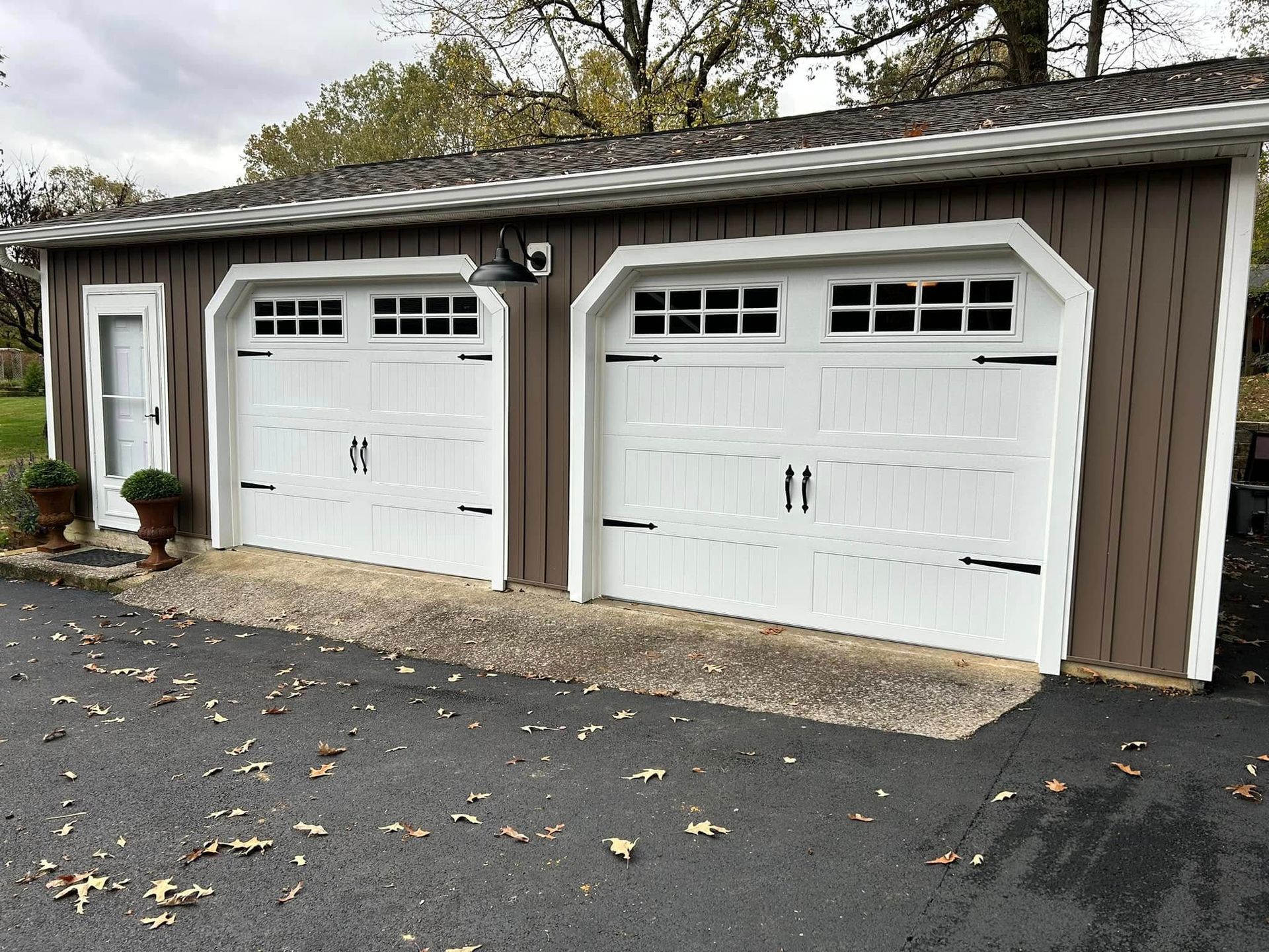 Two-car garage with white doors, dark trim, and brown siding. A small door is on the left.