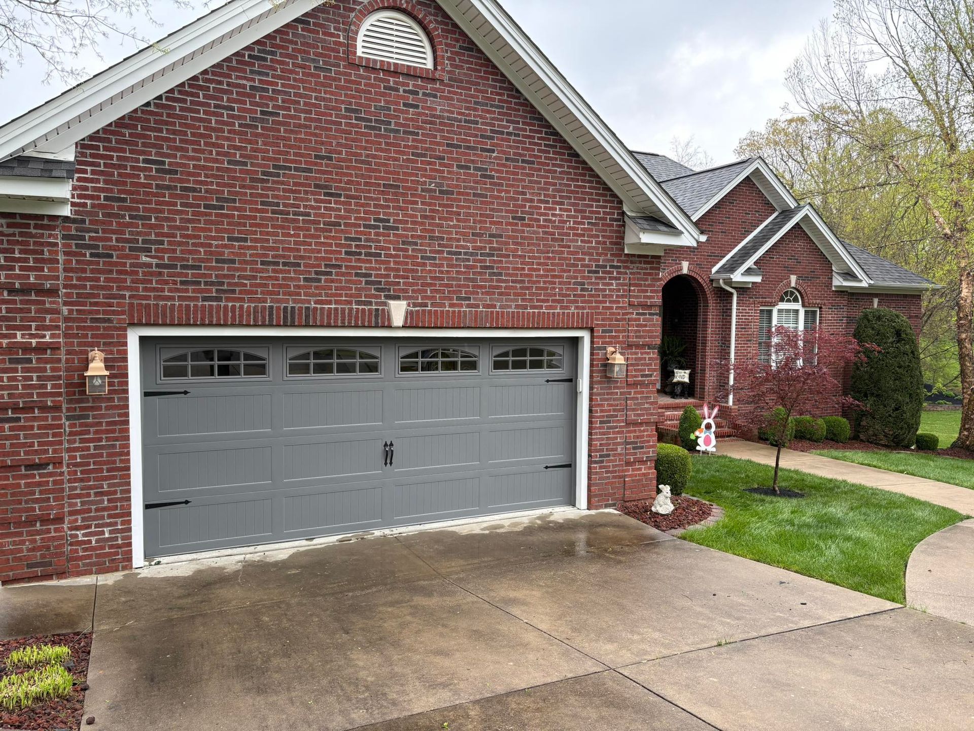 Brick house with a gray garage door, dark trim, and a curved walkway.