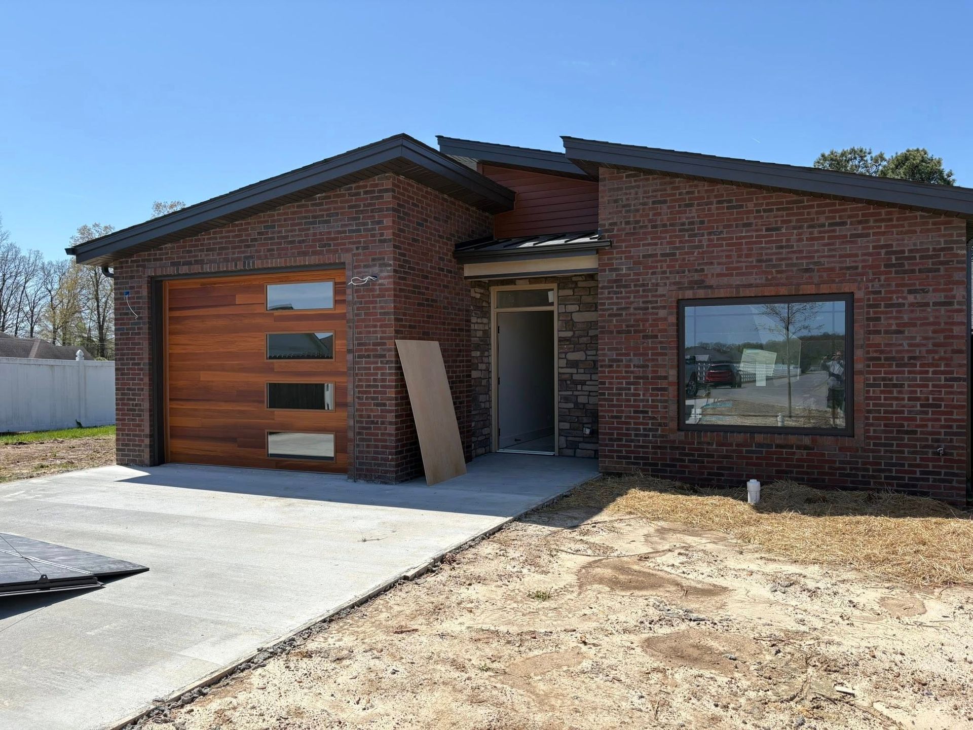 A modern, brick house with a wooden garage door and a concrete driveway, under a bright blue sky.